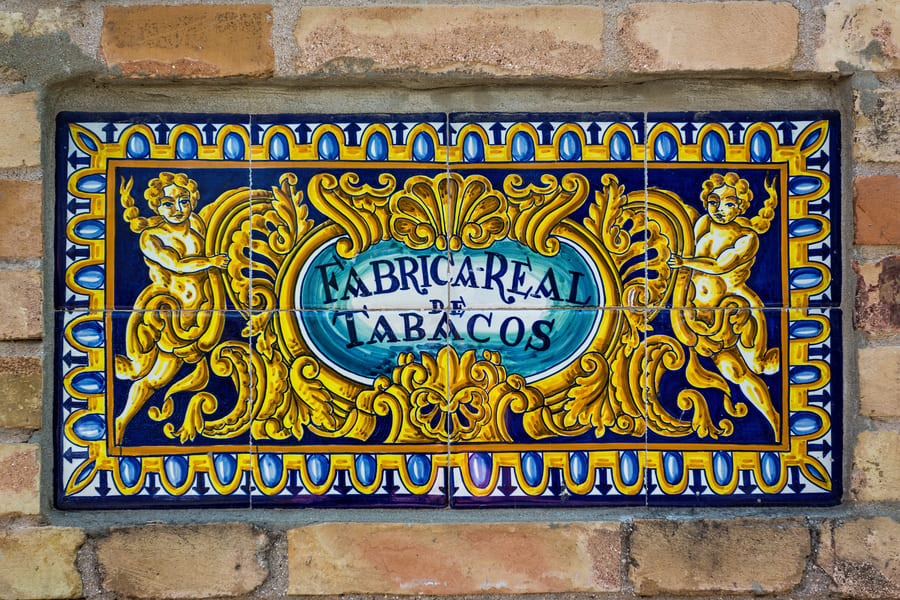 Carreaux de mur en briques portant l’inscription « FÁBRICA REAL DE TABACOS » et décorations ornementales, liées à la Fabrique Royale du Tabac de Séville, identité graphique urbaine.