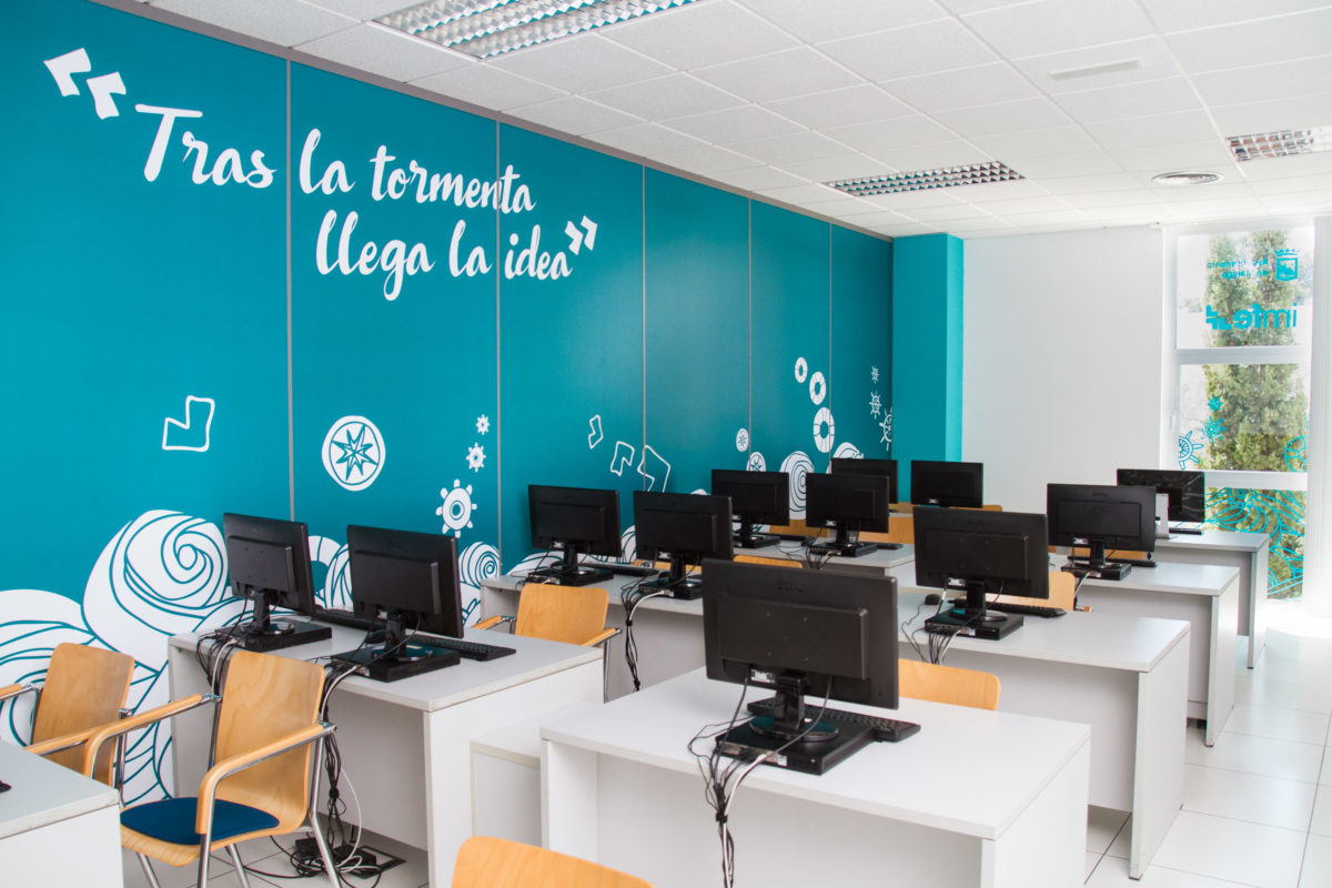 Salle informatique du projet IMFE avec une image de marque spatiale sur des murs turquoise, des phrases inspirantes en grand format et des stations informatiques réparties en rangées.